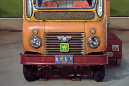 Orlando, Florida, USA - 11.15.2024: Closeup view of a vintage orange Sesame Street food truck with a NOM-NOM license plate. The headlights, grill, and bumper are lit by bright theme park lights at night.のeditorial素材