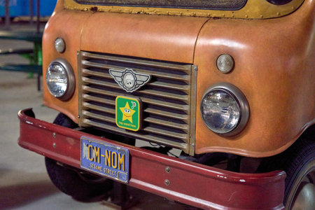 Orlando, Florida, USA - 11.15.2024: An angled closeup shows the front side of a vintage orange Sesame Street food truck with the NOM-NOM plate. The grill, headlights, and bumper glow under the theme park lights at night.のeditorial素材