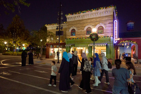 Orlando, Florida, USA - 11.15.2024: A group of families crosses a city street in front of festively decorated shops at night. Warm lights and Christmas garlands create a lively holiday atmosphere in the theme park.のeditorial素材