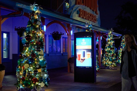 Orlando, Florida, USA - 11.15.2024: A row of small decorated Christmas trees glows outside a restaurant. A digital advertising screen lights the walkway with warm holiday colors.のeditorial素材