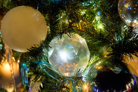 A faceted clear ornament and glossy baubles shine on a decorated evergreen. Warm lights and green needles create a festive night mood.の写真素材