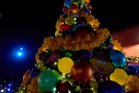 Orlando, Florida, USA - 11.15.2024: Close view of a Christmas tree decorated with large colorful baubles and yellow garland. Festive lights glow warmly against the dark night.のeditorial素材