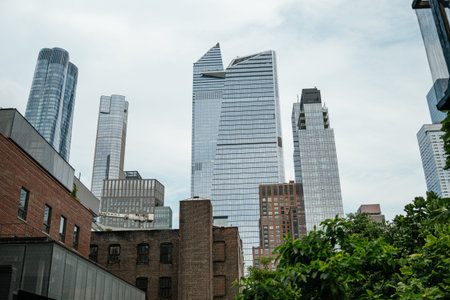 Modern glass towers rise behind historic brick buildings near the High Line in Manhattan. Green...