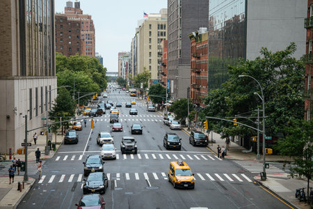 New York City, New York, USA - 08.02.2024: Traffic moves along a wide Manhattan avenue with yellow taxis, cars, and pedestrians crossing the street. Trees and mid-rise buildings line the busy urban roadway in New York City.のeditorial素材