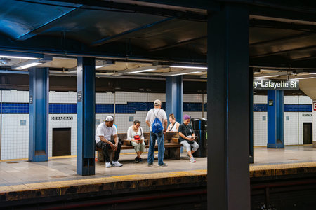New York City, New York, USA - 08.03.2024: Group of commuters waiting on the platform at Broadway Lafayette Street subway station in Manhattan. Urban underground transportation scene with tiled walls, blue columns, and railway tracks.のeditorial素材