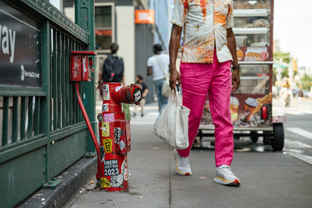 New York City, New York, USA - 08.03.2024: Red fire department standpipe covered with stickers near Broadway Lafayette subway entrance in Manhattan. Urban New York City sidewalk with pedestrian and street vendor in background.のeditorial素材