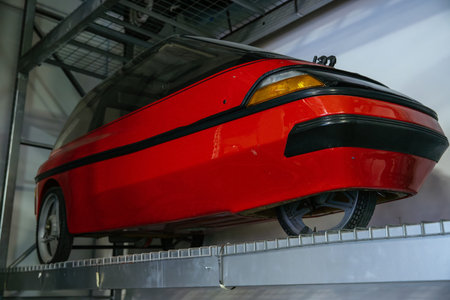 Striking red futuristic concept car showcased on metal display shelf in exhibition space. Vehicle features sleek, aerodynamic design with tinted glass canopy and prominent black trim line.