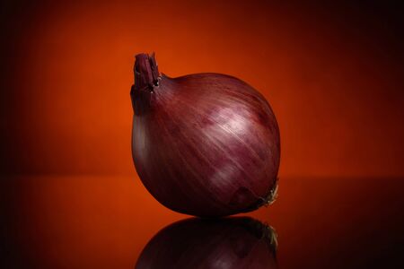 One red onion on a black and orange background with a reflection on the tableの写真素材