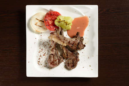 Barbecue beef ribs with grilled vegetables of tomato, onion and bell pepper on a square plate on a wooden table. Top view. Photos for restaurant and cafe menusの写真素材