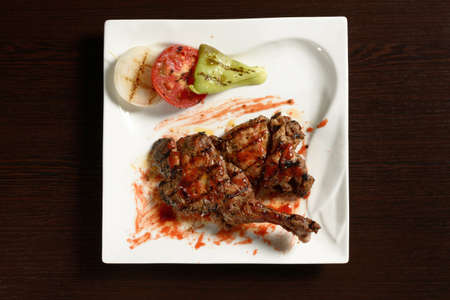 Barbecue chicken thigh with grilled vegetables of tomato, onion and bell pepper on a square plate on a wooden table. Top view. Photos for restaurant and cafe menusの写真素材