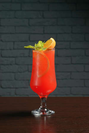 Red cold cocktail in a glass with orange and mint on a wooden table against a brick wall. Photos for restaurant, cafe and bar menusの写真素材