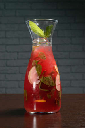 Glass decanter with a cold red fruit cocktail on ice on a wooden table against a brick wall. Photos for restaurant, cafe and bar menusの写真素材