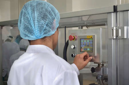 Pharmaceutical industry an employee in a dressing gown and headdress stands at the control panel of...