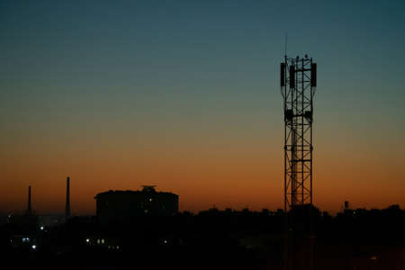 Night landscape, silhouette of city buildings and communication tower mobile operator antenna...