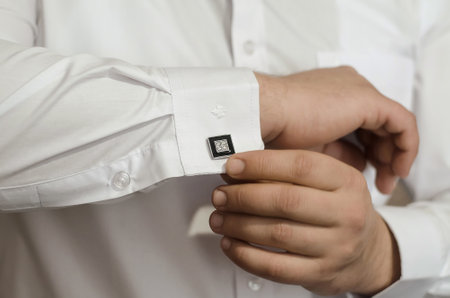 Groom's hands fasten the black cufflinks on his shirt, close-up. The preparations of the groom