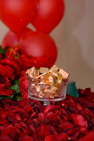 Bowl of candy wrapped in gold on the table in the middle of rose petalsの写真素材