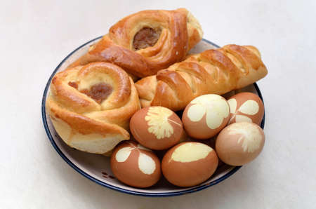 Rich sweet buns with jam and easter eggs with leaf patterns on the plate