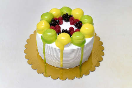 White meringue cake with whipped cream, decorated with green and yellow balls and berries, on a white tableの写真素材