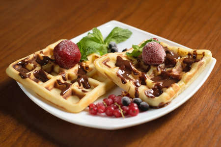 Two large waffles poured with chocolate, with frozen strawberries and berries on a white plateの写真素材