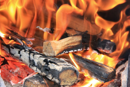 Large bonfire close-up, flames of fire, charred pieces of wood logs and ashes