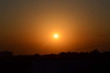 Beautiful sunset with an orange sky with silhouettes of trees and houses in the cityの写真素材