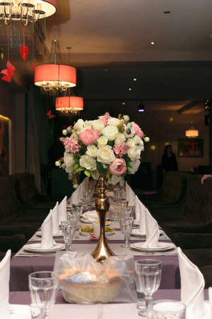 Beautifully served table in a restaurant with a bouquet of white and pink flowers in a golden vaseの写真素材
