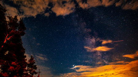 The Milky Way Galaxy, the trail from an airplane, Jupiter, Saturn and many stars in the night sky. Forest, power line and clouds. Cosmic landscape.の写真素材