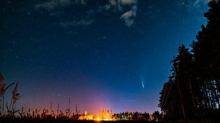 A beautiful comet C/2020 F3 (NEOWISE) with two tails surrounded by many stars in the night sky. A cosmic landscape with a field, a forest and a power line.の写真素材