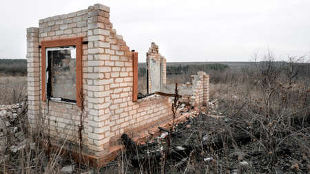 Destroyed and burnt brick structure with a window at the edge of the fieldの写真素材