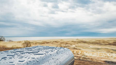 Wet metal surface against a background of sand dunes and overcast sky.