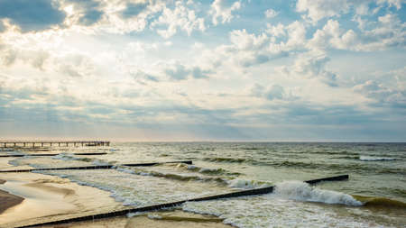 Wavy Baltic Sea before sunset, Zelenogradsk pier and breakwaters near the shore, sun rays breaking...