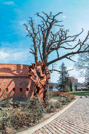 Strange rusty figure under a tree without leaves against a brick wallの写真素材