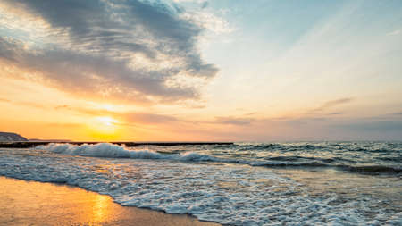 Sunset in the wavy sea with a wooden breakwater by the sandy shore, evening seascapeの写真素材