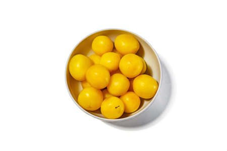 Lots of yellow plums in a white deep dish on a white background, view from aboveの写真素材