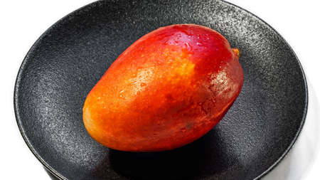 Fresh juicy red-orange mango on a black plate isolated on a white background, close-upの写真素材