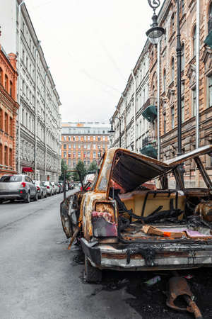 A burnt-out, rusted-out car on the street of a European city, vertical photoの写真素材