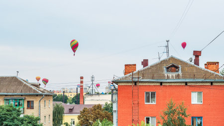 Many colorful balloons fly in the sky above the roofs of high-rise buildings in a provincial cityの写真素材