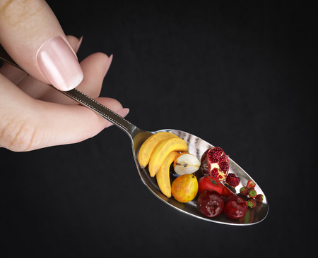 woman hand holding spoon with fruits on isolate black diet concept photo closeupの写真素材