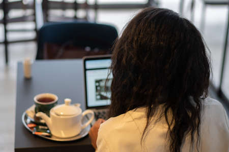 Young businesswoman drinking tea and using tablet computer in cafe. Back view.の写真素材