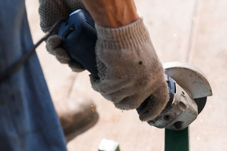 Builder worker with grinder machine cutting metal wood at construction site