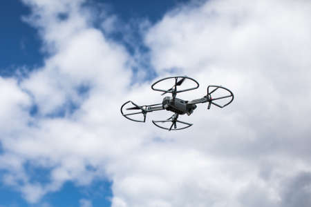 Quadrocopter against the blue sky with white clouds. The flight of the copter in the sky