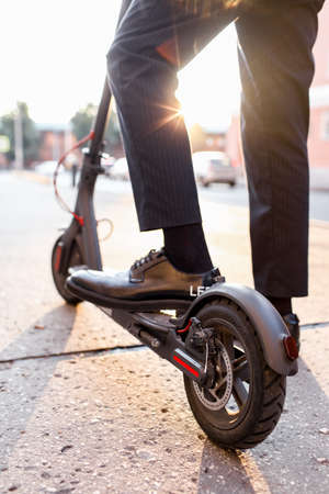 Legs of a man in stylish outfit stand on electric scooter on the streetの写真素材