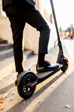 Legs of a man in stylish outfit stand on electric scooter on the street