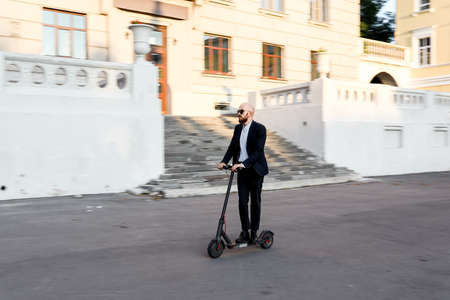 Attractive business man riding a kick scooter at cityscape backgroundの写真素材