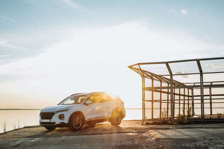 White compact SUV car with sport and modern design parked on concrete road by the sea near the beach at sunsetの写真素材