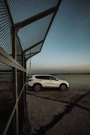 White compact SUV car with sport and modern design parked on concrete road by the sea near the beach at sunsetの写真素材