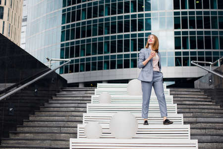 Side view of mature woman in business suit walking back to home talking on phone. Senior businesswoman using cellphone on city street with urban backgroundの写真素材