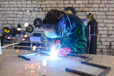 welder in a welding mask and welders leathers, a metal product is welded with a welding machine in...
