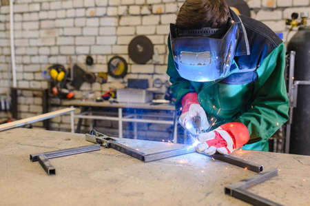 welder in a welding mask and welders leathers, a metal product is welded with a welding machine in...