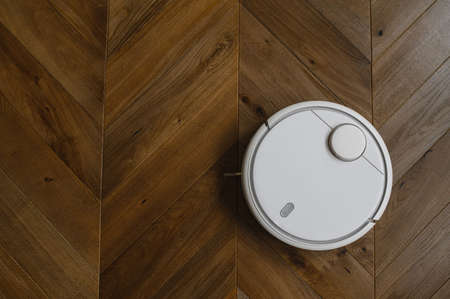 Robotic vacuum cleaner on laminate wood floor in bedroom.